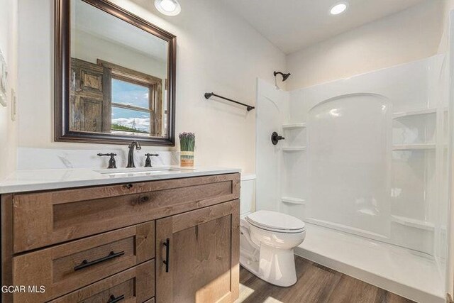 bathroom with a shower, hardwood / wood-style floors, vanity, and toilet