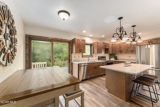 kitchen with appliances with stainless steel finishes, light wood-type flooring, pendant lighting, an inviting chandelier, and a kitchen island