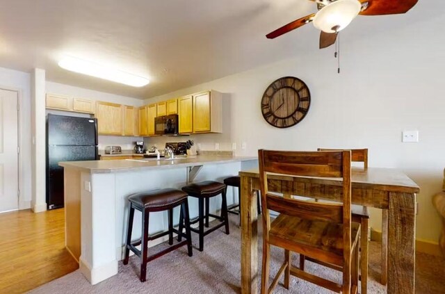 kitchen with light countertops, light brown cabinetry, black appliances, a peninsula, and a kitchen breakfast bar