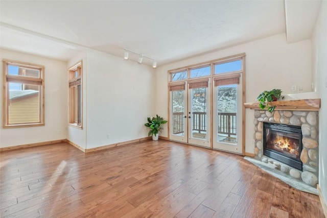 unfurnished living room with track lighting, a stone fireplace, and hardwood / wood-style floors