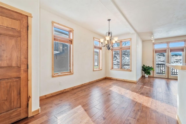 unfurnished dining area with a chandelier, a wealth of natural light, and light wood-type flooring