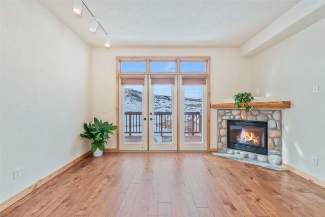 unfurnished living room with a stone fireplace, light hardwood / wood-style floors, and rail lighting