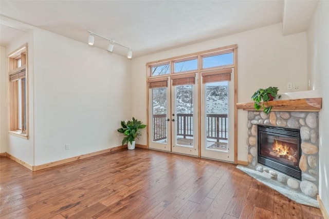 unfurnished living room with a stone fireplace, hardwood / wood-style floors, and track lighting