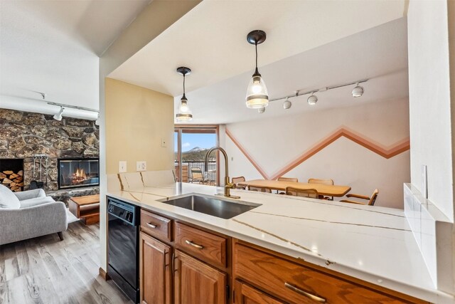 kitchen featuring sink, pendant lighting, dishwasher, light hardwood / wood-style floors, and a stone fireplace