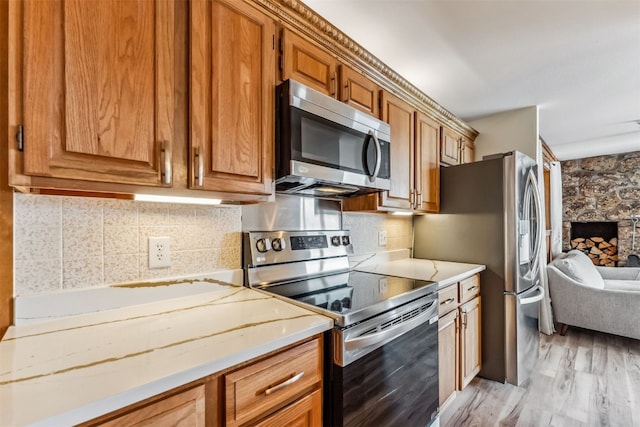 kitchen featuring tasteful backsplash, a stone fireplace, light hardwood / wood-style flooring, and appliances with stainless steel finishes