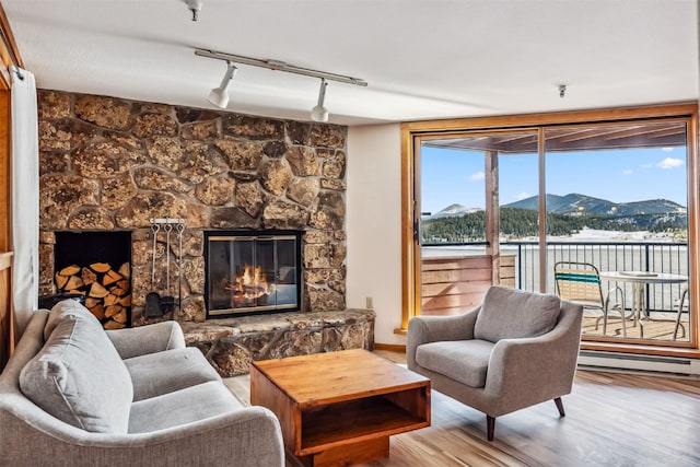 living room featuring rail lighting, a baseboard radiator, a stone fireplace, a mountain view, and light wood-type flooring