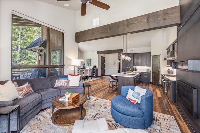 living room with ceiling fan with notable chandelier, lofted ceiling with beams, sink, and dark wood-type flooring