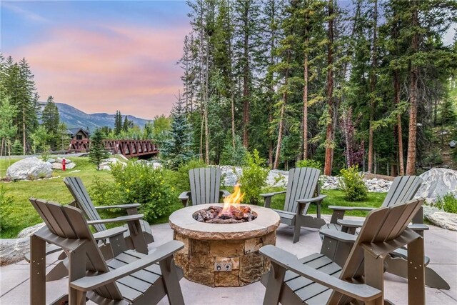 patio terrace at dusk featuring a mountain view, a yard, and a fire pit