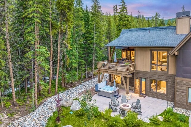 back house at dusk with a patio area, a wooden deck, and a fire pit