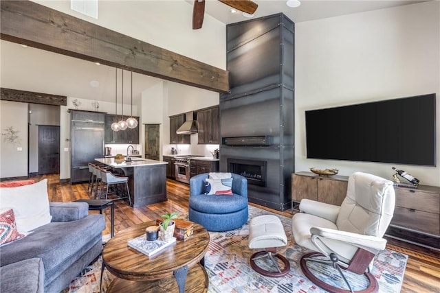 living room with a large fireplace, dark hardwood / wood-style flooring, sink, and a high ceiling