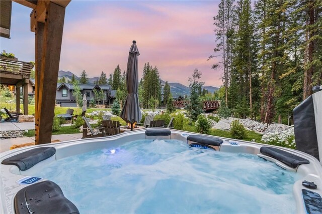 pool at dusk with a mountain view and a hot tub