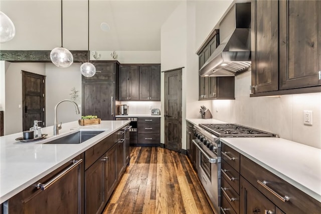 kitchen featuring dark brown cabinetry, sink, hanging light fixtures, wall chimney range hood, and high end range