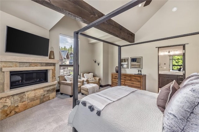 carpeted bedroom featuring ceiling fan, sink, lofted ceiling with beams, connected bathroom, and a stone fireplace