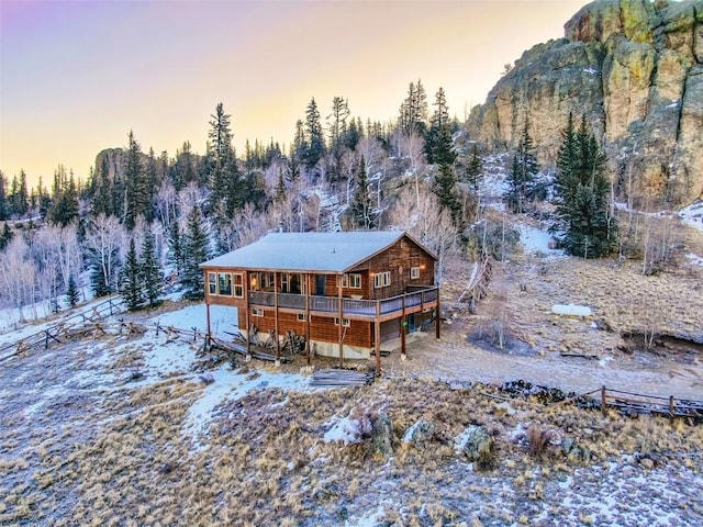 snow covered rear of property with a forest view and a wooden deck