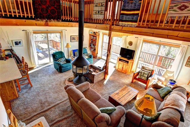 living room featuring carpet floors, a wood stove, a wealth of natural light, and a towering ceiling