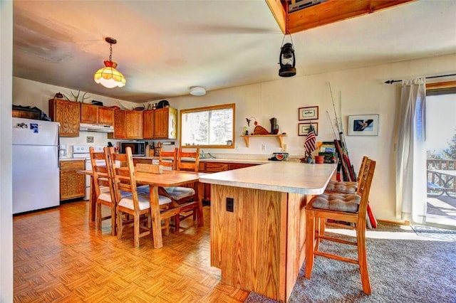 kitchen with kitchen peninsula, pendant lighting, white appliances, a breakfast bar area, and light parquet flooring