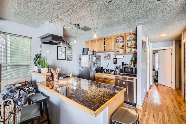 kitchen with a breakfast bar, a textured ceiling, light wood-type flooring, appliances with stainless steel finishes, and kitchen peninsula