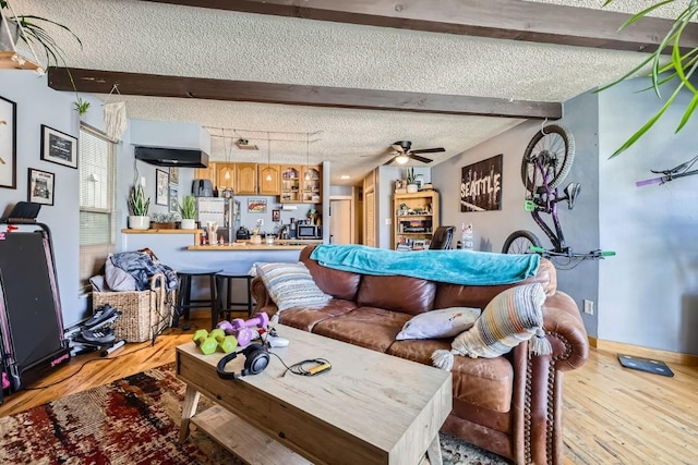 living room featuring beamed ceiling, ceiling fan, a textured ceiling, and light hardwood / wood-style flooring