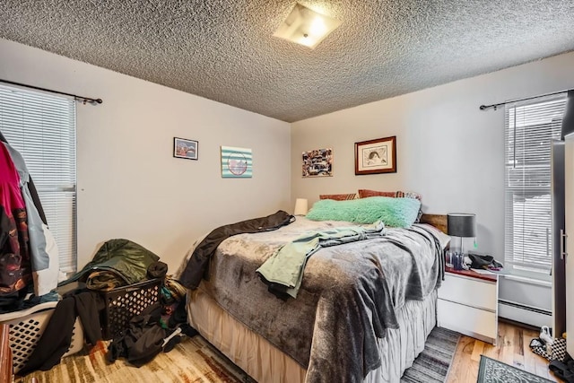 bedroom featuring hardwood / wood-style flooring, a baseboard heating unit, and a textured ceiling