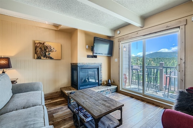 living room with a textured ceiling, dark hardwood / wood-style flooring, beamed ceiling, wooden walls, and a fireplace