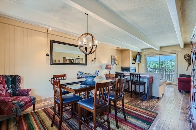 dining space with an inviting chandelier, wooden walls, wood-type flooring, a textured ceiling, and beam ceiling