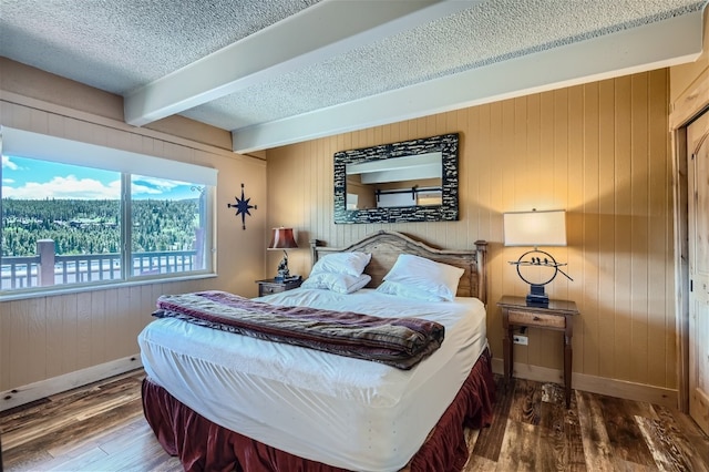 bedroom featuring beam ceiling, wood walls, a textured ceiling, and hardwood / wood-style floors