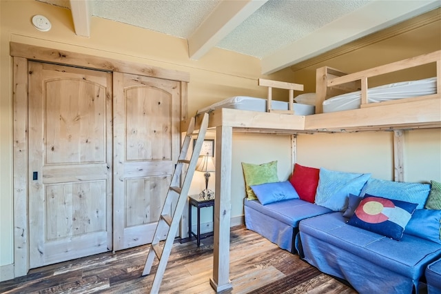 bedroom with a textured ceiling, beam ceiling, and hardwood / wood-style flooring