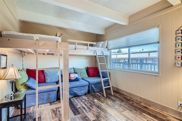 bedroom with a textured ceiling, beam ceiling, hardwood / wood-style floors, and wooden walls