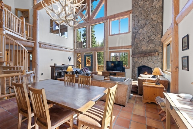 dining space with a stone fireplace, a towering ceiling, light tile patterned floors, and a chandelier