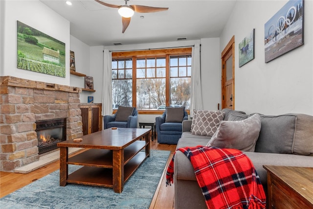 living room with wood-type flooring, a stone fireplace, and ceiling fan