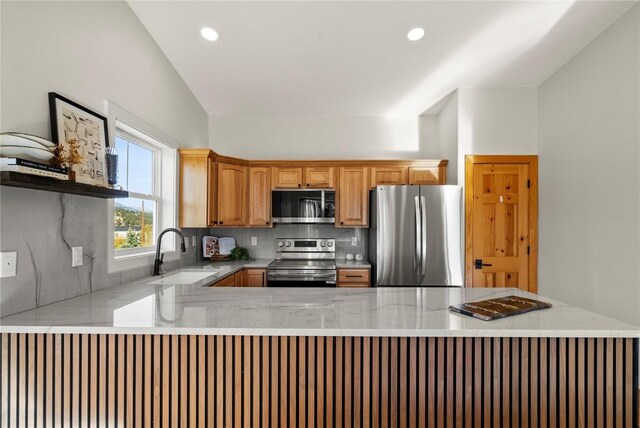 kitchen featuring lofted ceiling, backsplash, sink, light stone counters, and stainless steel appliances