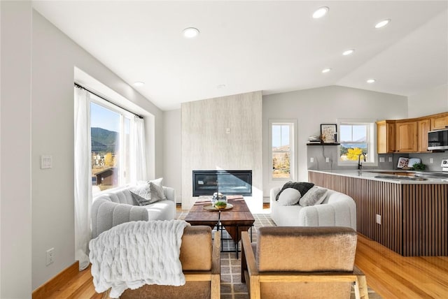 living room featuring a fireplace, light hardwood / wood-style flooring, lofted ceiling, and sink