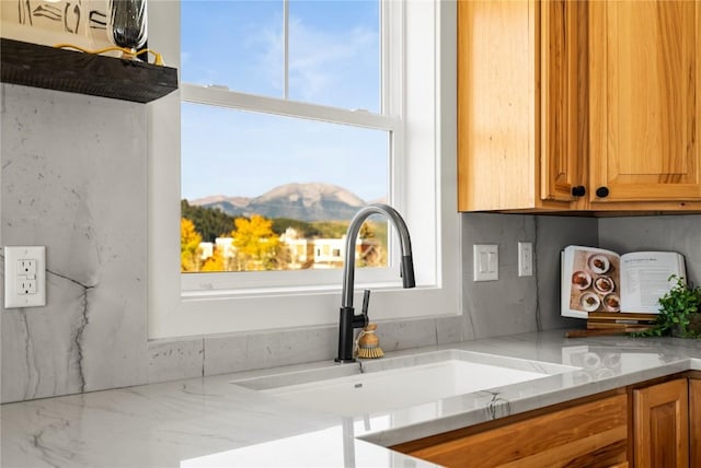 details featuring a mountain view, tasteful backsplash, light stone counters, and sink