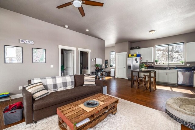 living room with baseboards, a ceiling fan, dark wood-style flooring, and a textured ceiling