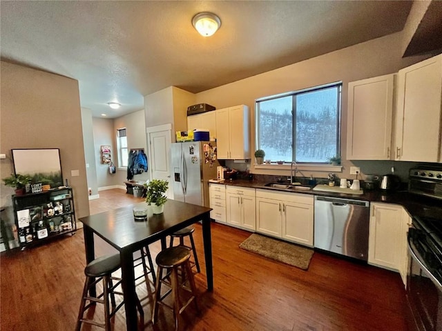 kitchen with a sink, dark countertops, appliances with stainless steel finishes, and dark wood-style floors