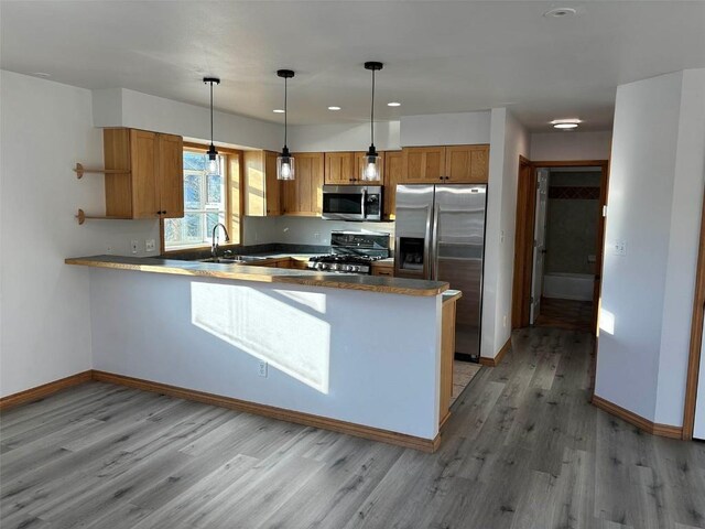 kitchen featuring kitchen peninsula, stainless steel appliances, sink, light hardwood / wood-style flooring, and hanging light fixtures