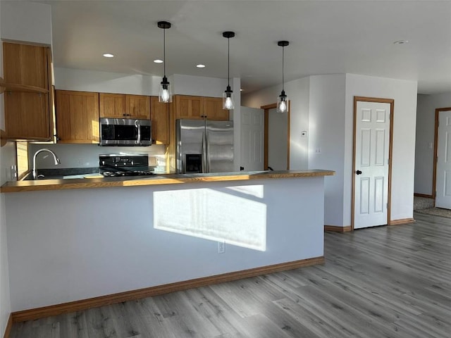 kitchen featuring sink, kitchen peninsula, pendant lighting, appliances with stainless steel finishes, and hardwood / wood-style flooring