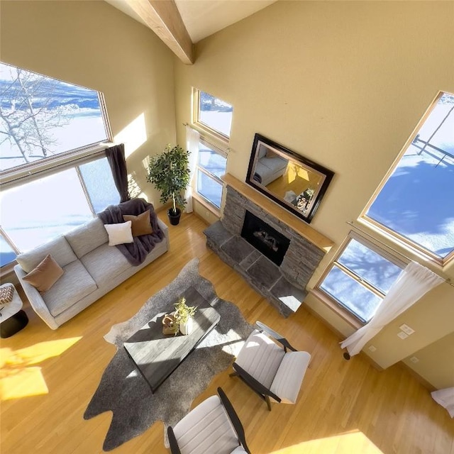 living room featuring beam ceiling, a stone fireplace, wood-type flooring, and a towering ceiling