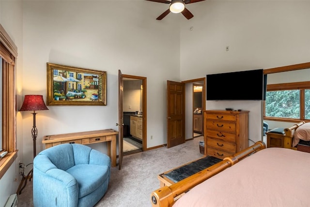 carpeted bedroom featuring baseboard heating, ceiling fan, a towering ceiling, and ensuite bathroom