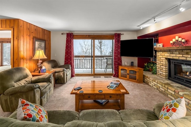 carpeted living room with a fireplace, track lighting, and wood walls