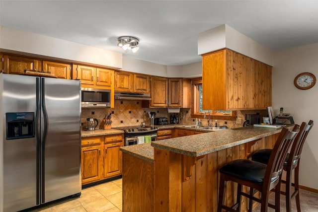 kitchen with kitchen peninsula, stainless steel appliances, sink, dark stone countertops, and decorative backsplash