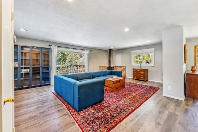 living room with recessed lighting, a wood stove, a textured ceiling, wood finished floors, and baseboards