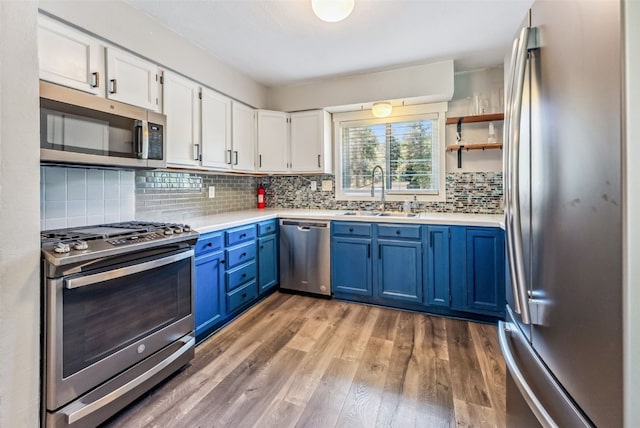 kitchen with blue cabinets, a sink, appliances with stainless steel finishes, white cabinets, and light wood finished floors