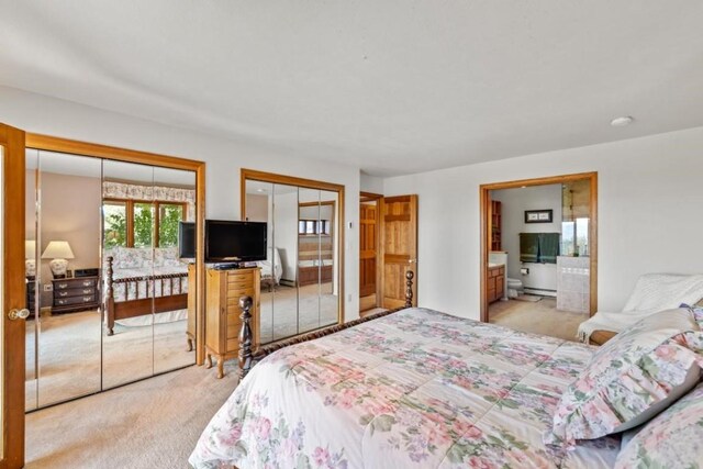 bedroom featuring multiple closets, ensuite bath, and light carpet