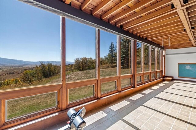 unfurnished sunroom with a mountain view, a wealth of natural light, and wooden ceiling