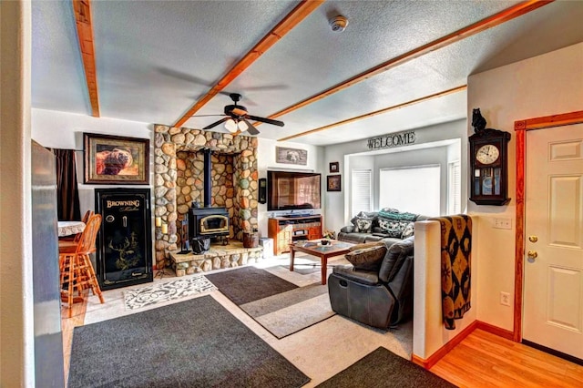 living room featuring a wood stove, ceiling fan, a textured ceiling, and light wood-type flooring