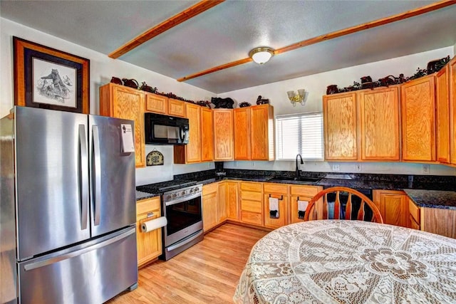 kitchen with dark stone counters, sink, light wood-type flooring, a textured ceiling, and stainless steel appliances