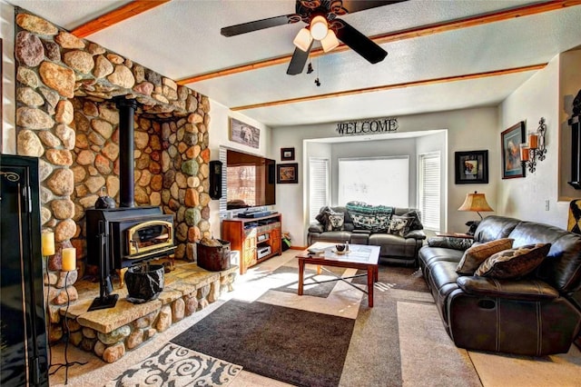 carpeted living room with a wood stove, ceiling fan, beamed ceiling, and a textured ceiling