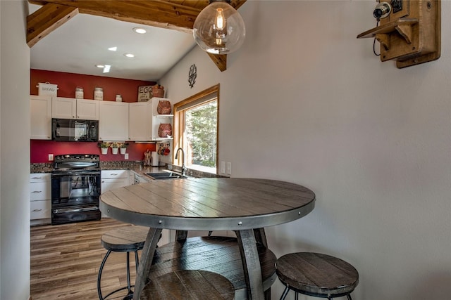 kitchen featuring sink, vaulted ceiling with beams, hardwood / wood-style floors, white cabinets, and black appliances