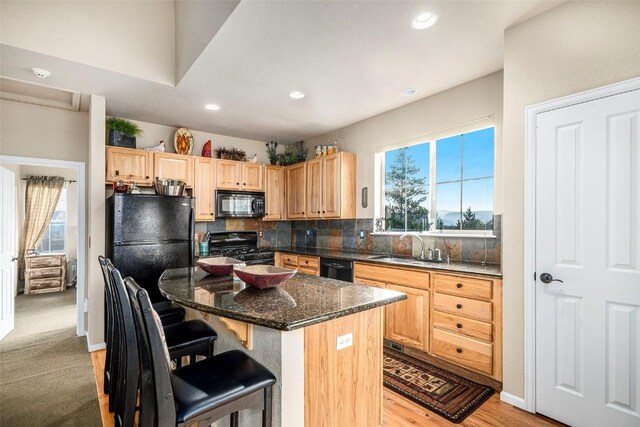 kitchen featuring a kitchen bar, dark stone counters, sink, black appliances, and a kitchen island